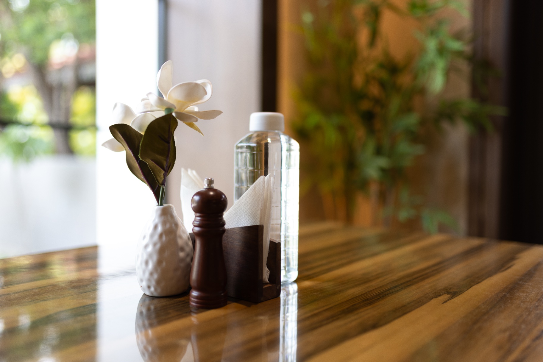 D'Scops Café table detail with flower vase, water bottle, pepper mill, and warm wooden tabletop
