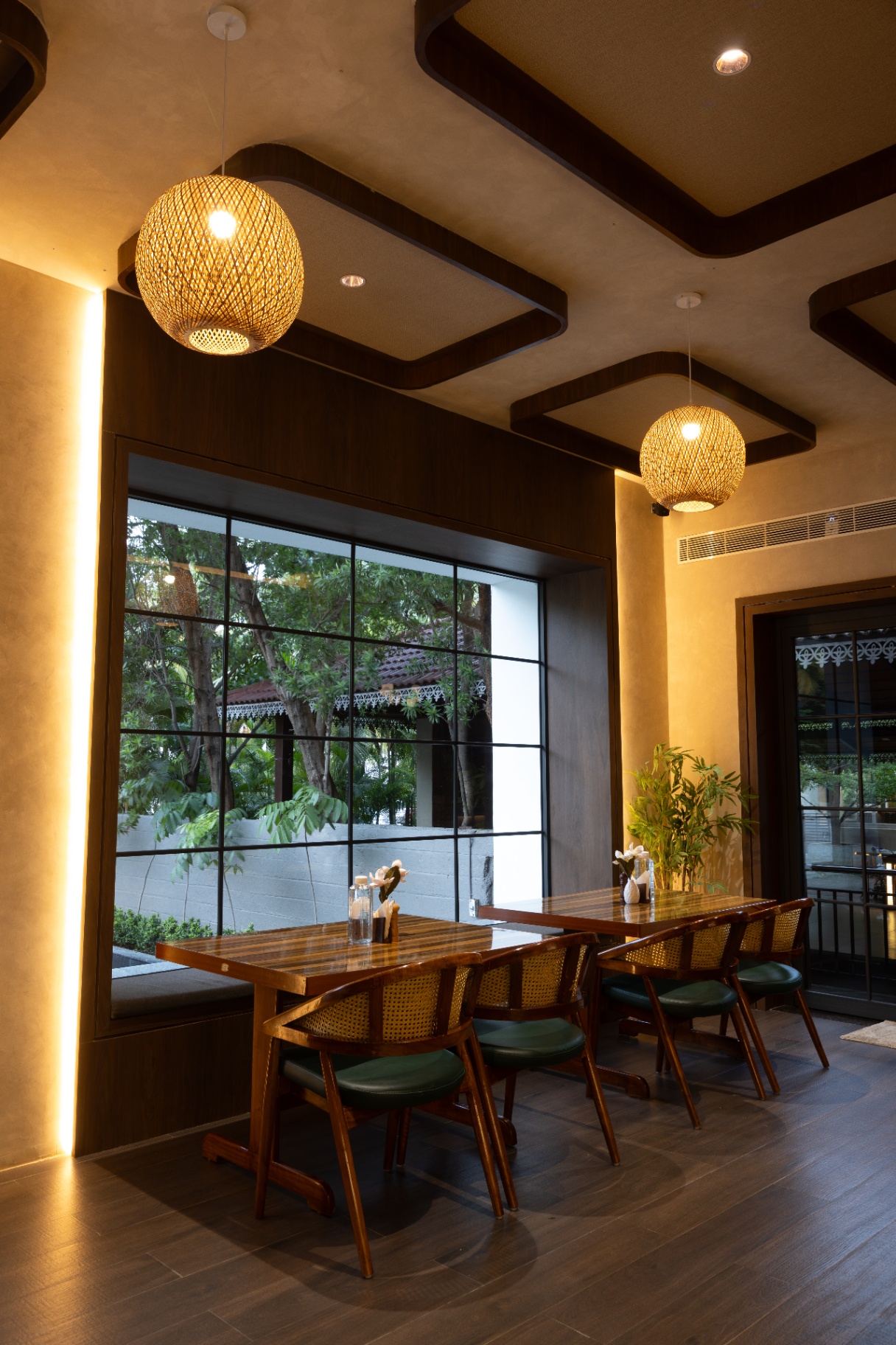 D'Scops Café window-side seating with cane chairs, pendant lamps, warm columns, and café greenery