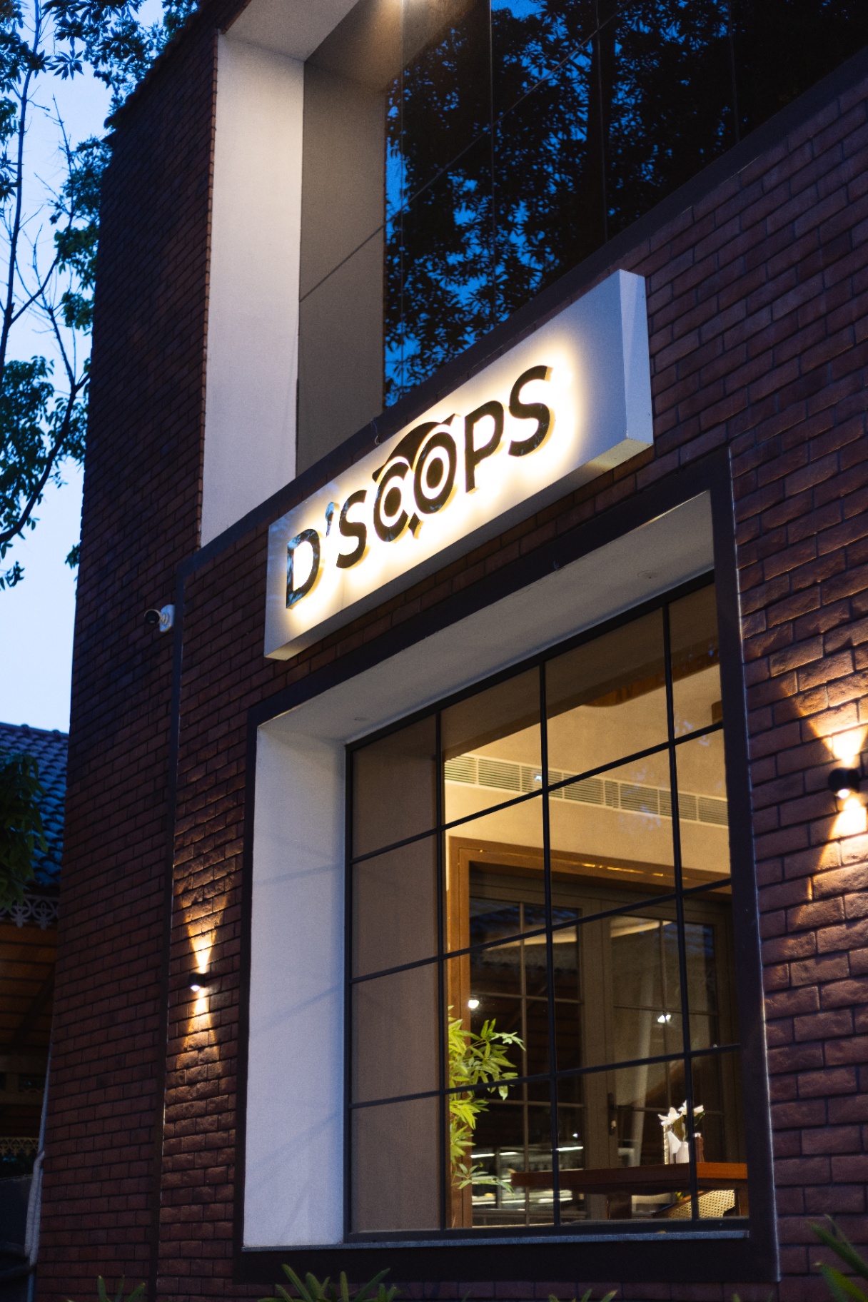 D'Scops Café exterior window signage with brick wall, warm lights, and visible café interior