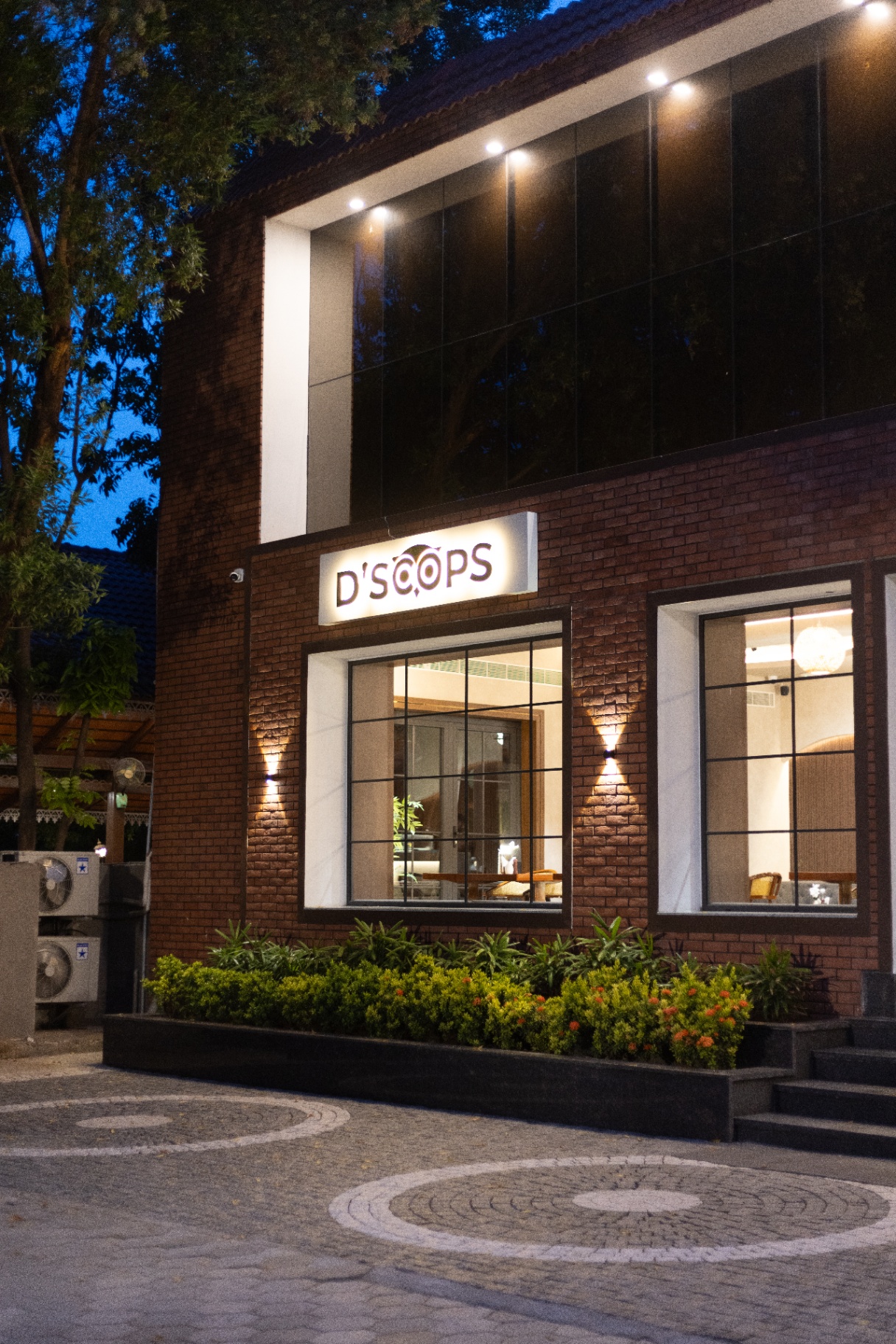 D'Scops Café evening facade angle with illuminated sign, brick exterior, and warm windows