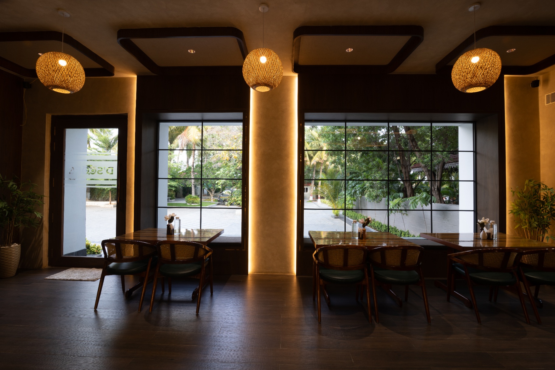 D'Scops Café wide interior seating with warm columns, large windows, cane chairs, and pendant lighting